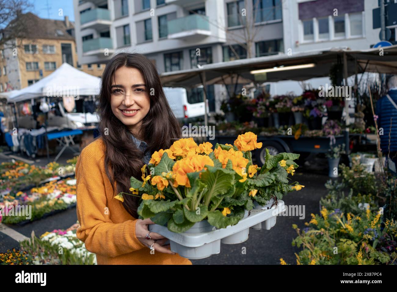Donna sorridente che tiene una cassa di fiori in piedi al mercato Foto Stock