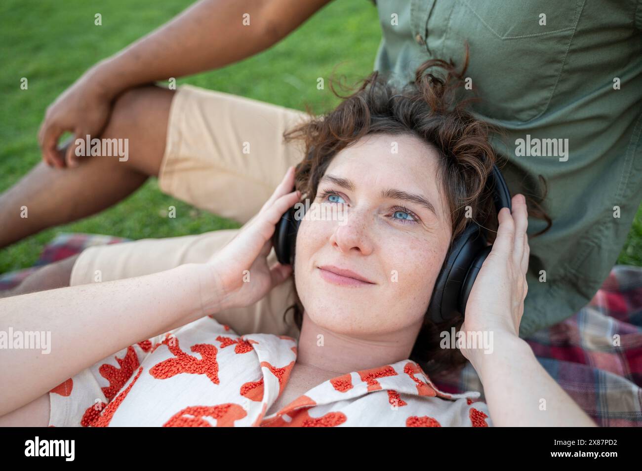Donna sorridente che ascolta la musica con le cuffie wireless e si sdraia in grembo al ragazzo Foto Stock