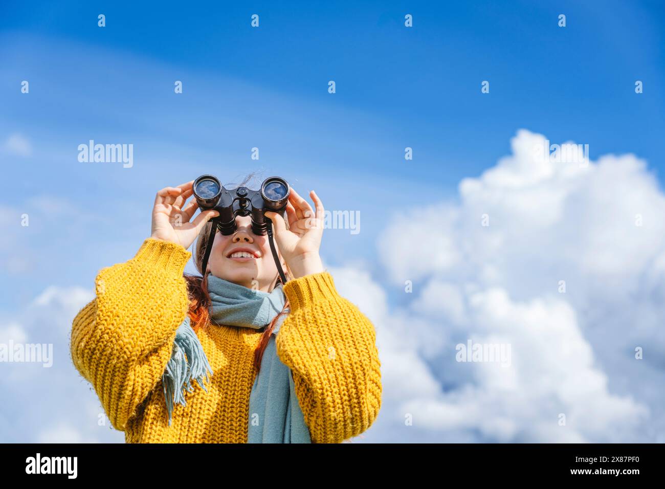 Ragazza felice che guarda attraverso il binocolo sotto il cielo nuvoloso Foto Stock