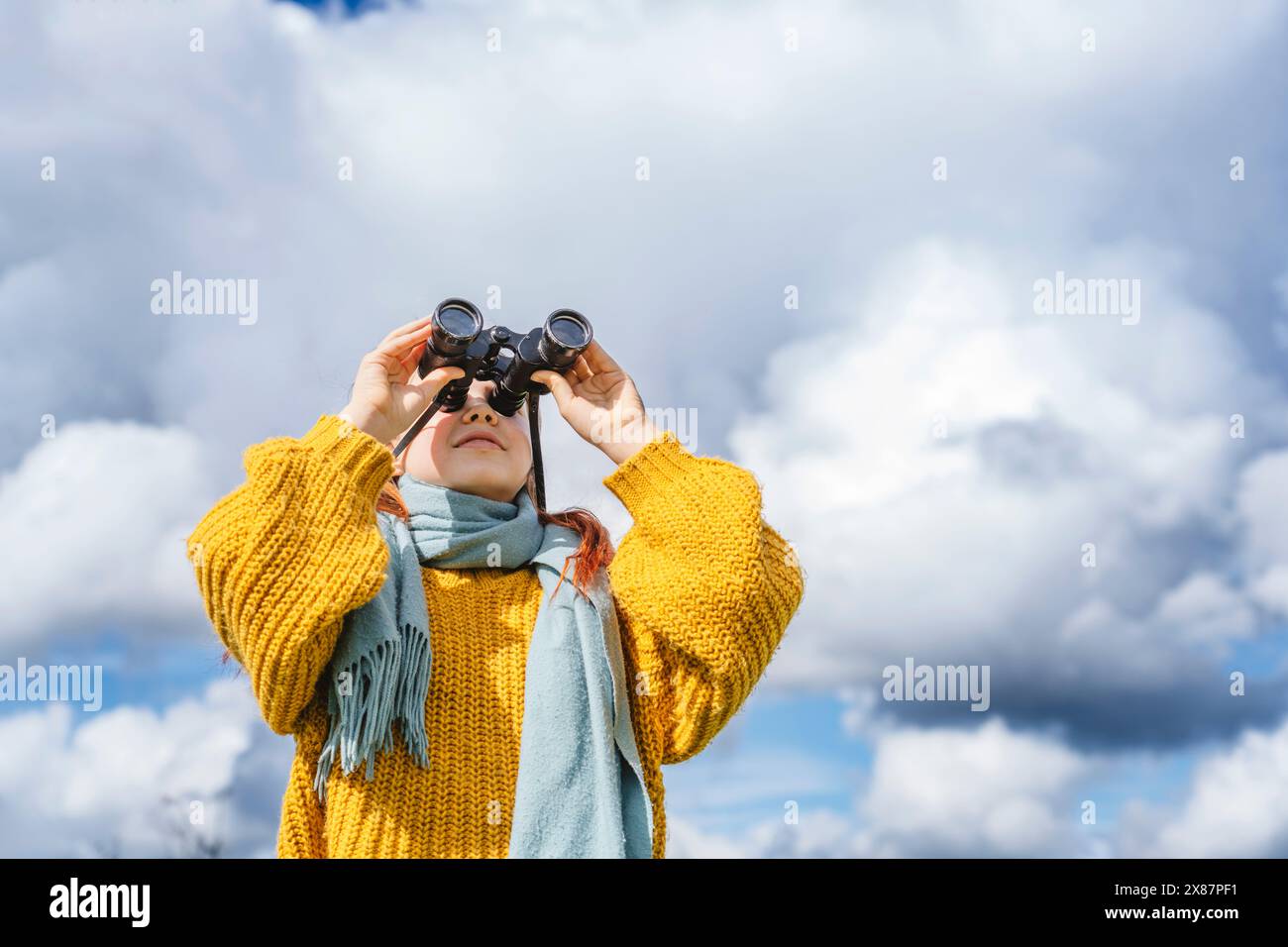 Ragazza sorridente che guarda attraverso un binocolo sotto il cielo nuvoloso Foto Stock
