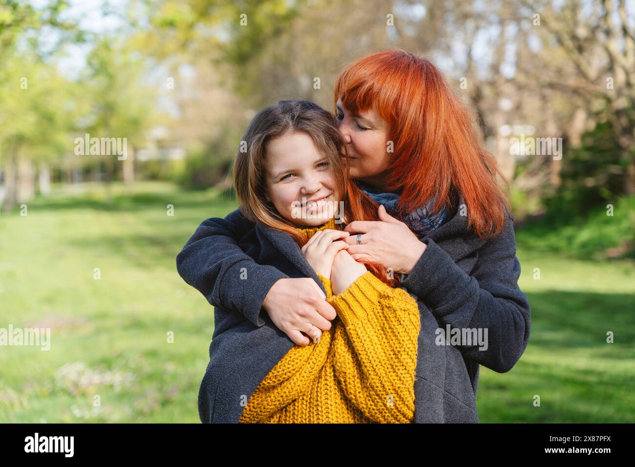 Madre sorridente che baciava e si prendeva cura della figlia il giorno di sole al parco Foto Stock