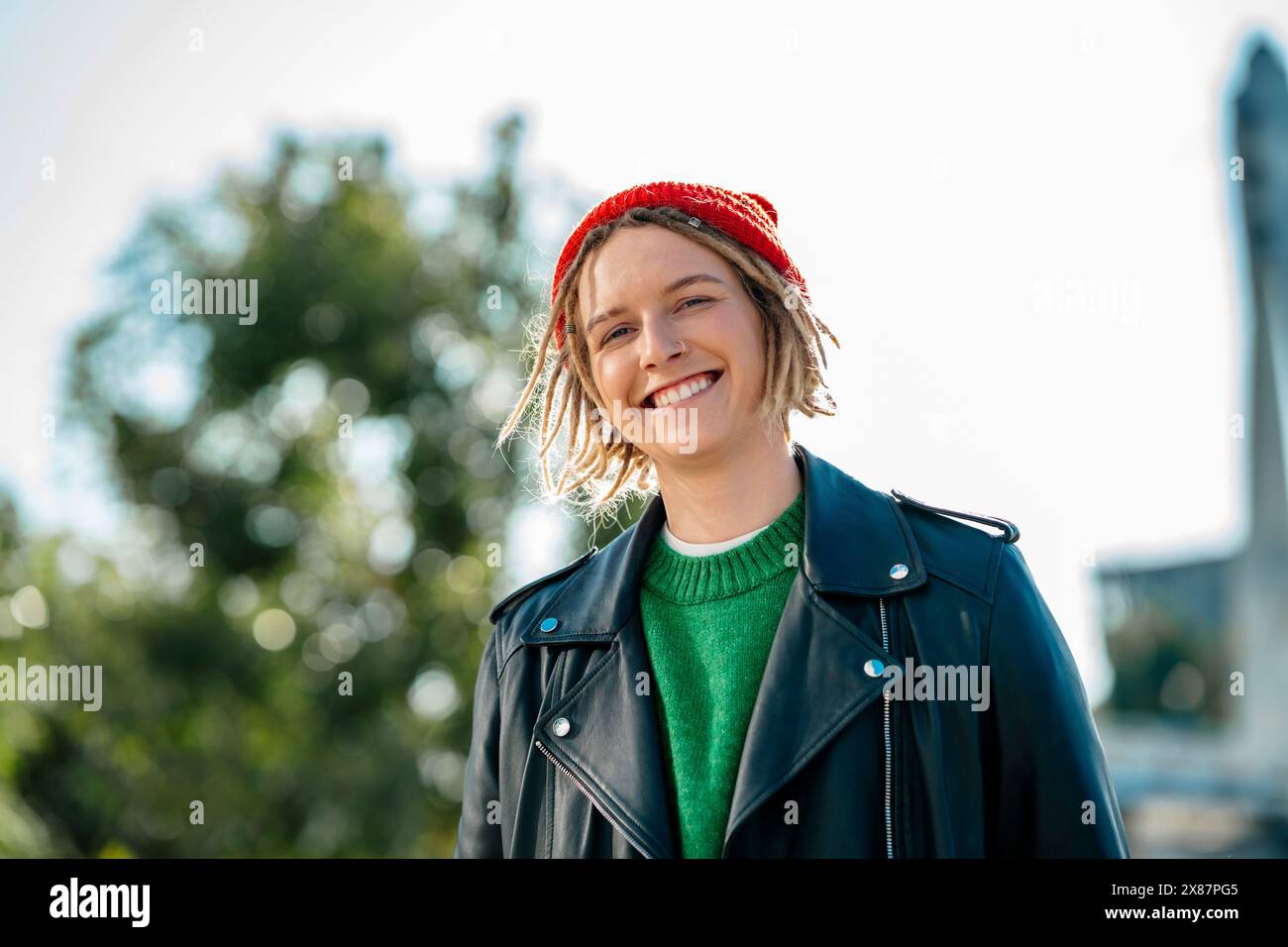 Giovane donna sorridente che indossa un cappello in maglia e una giacca in pelle Foto Stock