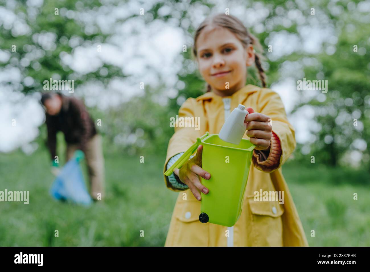 Una ragazza sorridente che mette una bottiglia di plastica giocattolo nel bidone della spazzatura Foto Stock