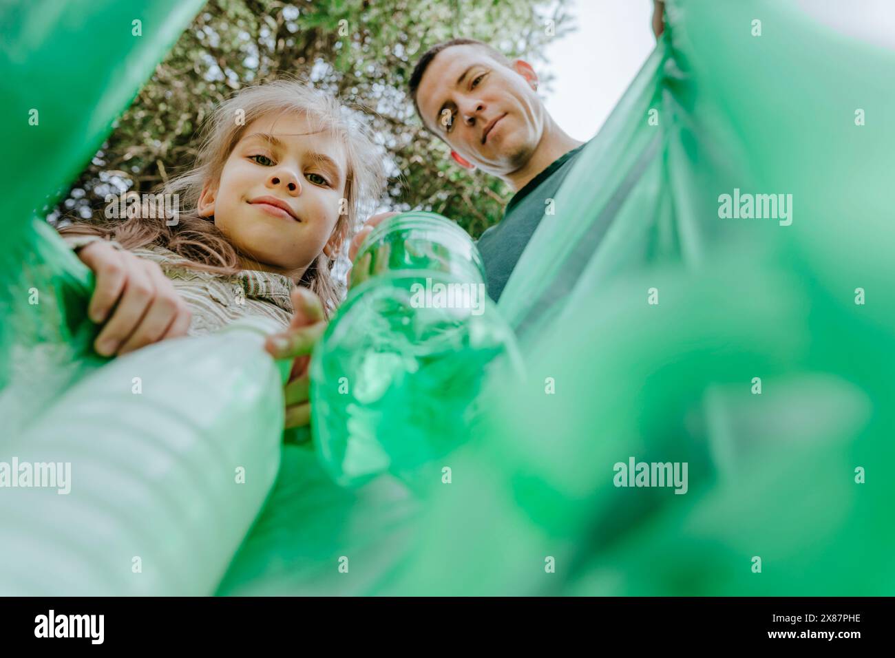 Padre e figlia sorridenti che raccolgono bottiglie di plastica in un sacchetto della spazzatura Foto Stock