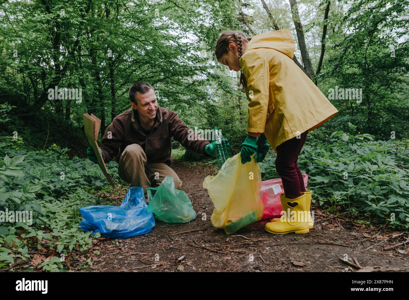 Padre e figlia sorridenti che raccolgono rifiuti in sacchetti multicolore Foto Stock