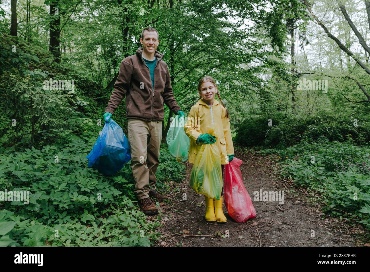 Padre e figlia felici in piedi con i sacchi della spazzatura nella foresta Foto Stock