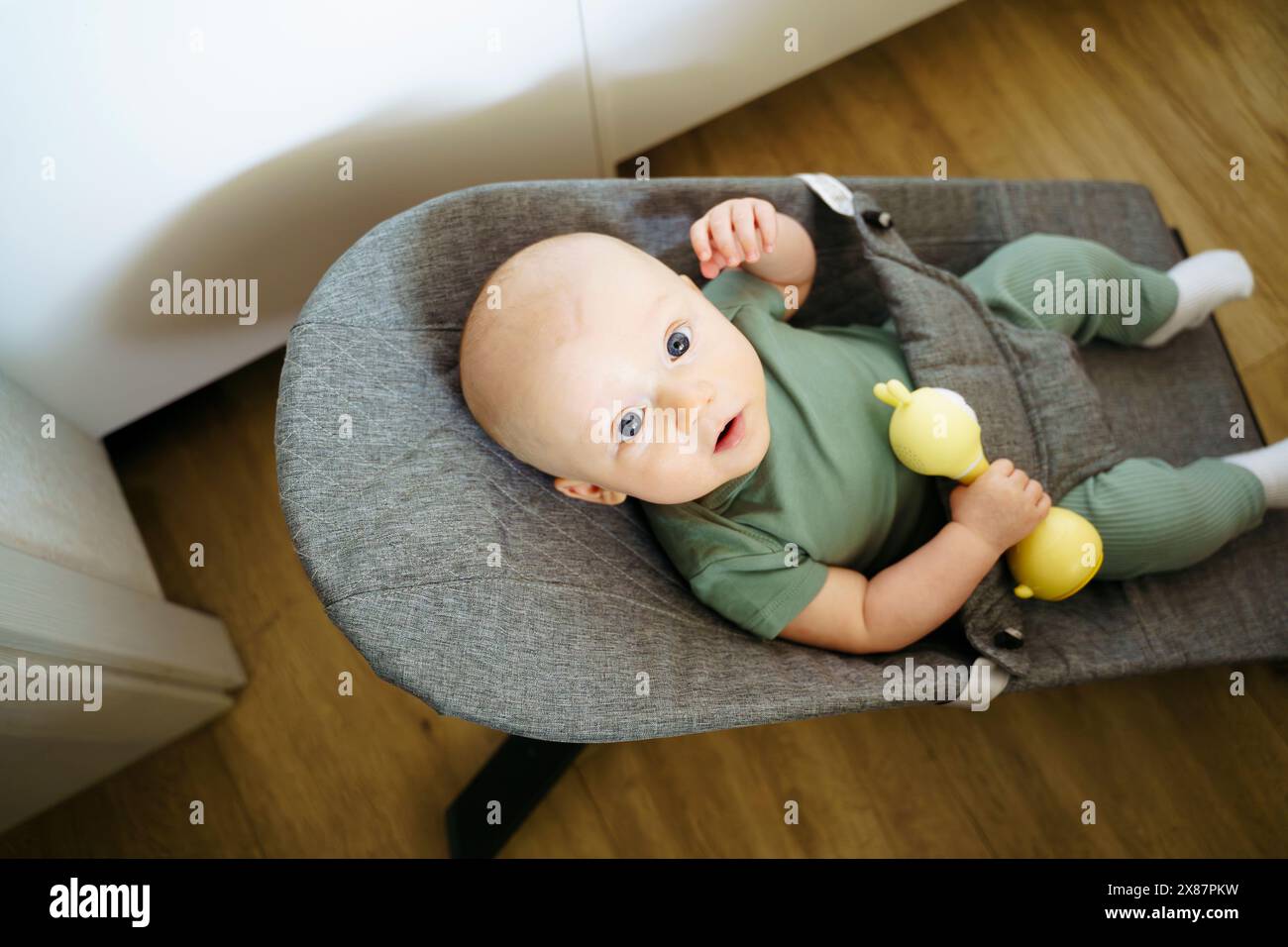 Bambino carino e con un giocattolo giallo seduto su una sedia a dondolo Foto Stock