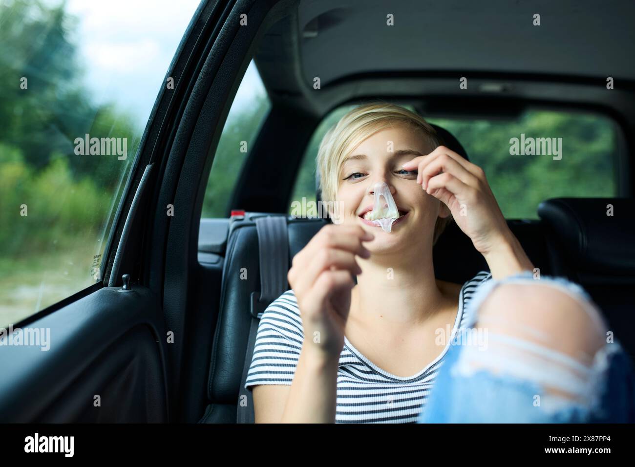 Giovane donna sorridente che mangia gomma da bolla seduta in macchina Foto Stock