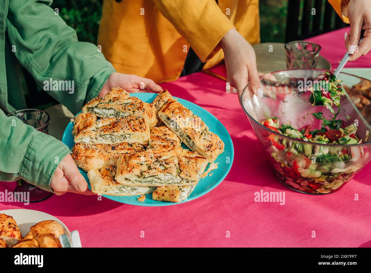 Mani di donne che servono insalata verde e pane ripieno al formaggio a tavola Foto Stock