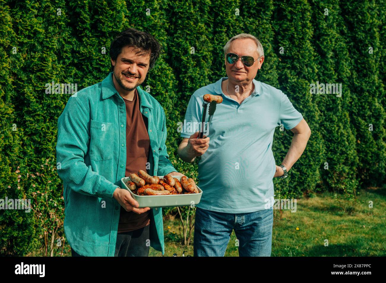 Padre e figlio felici in piedi con salsicce cotte nel cortile posteriore Foto Stock