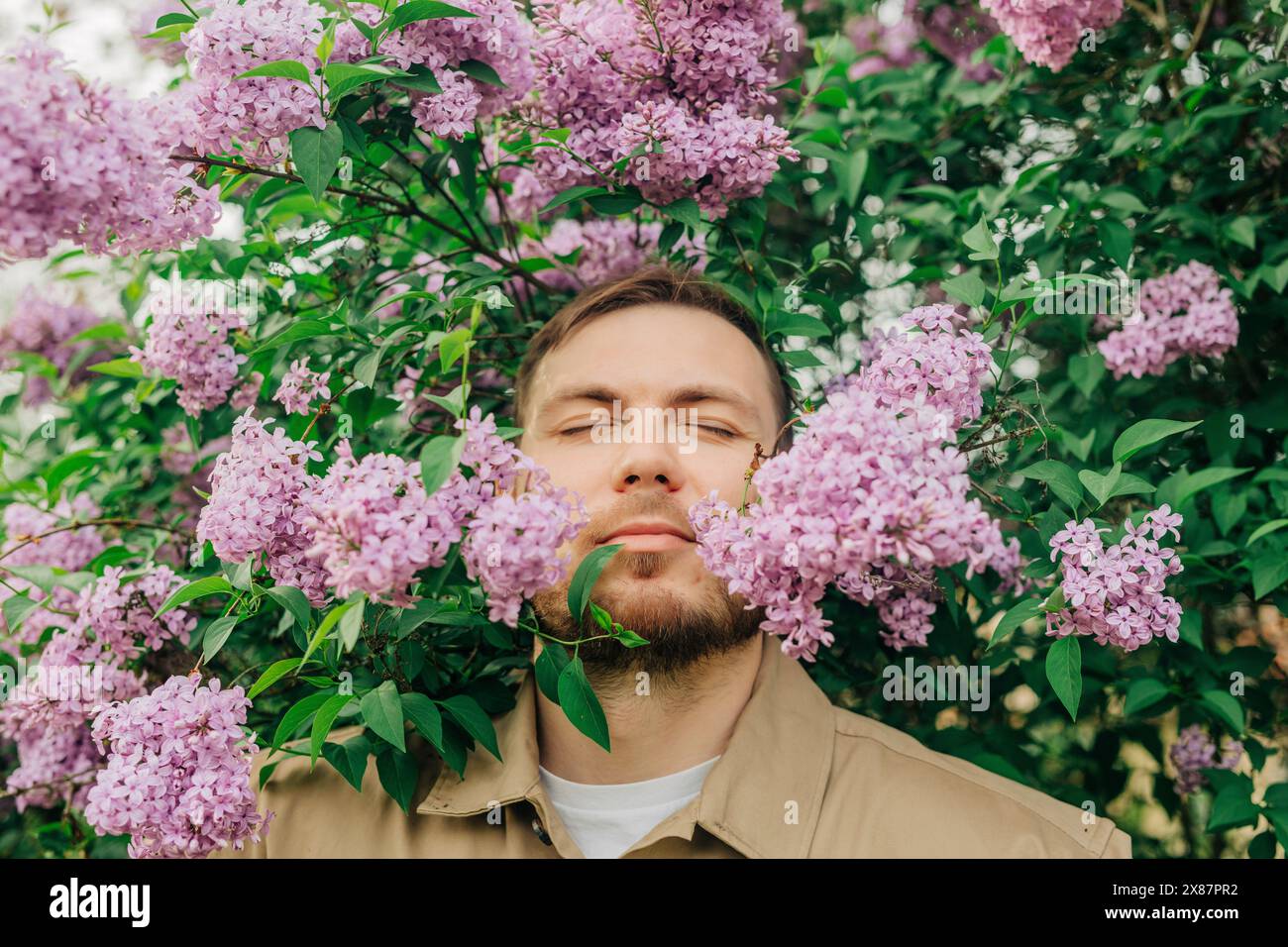 Uomo sorridente tra fiori lilla in giardino Foto Stock
