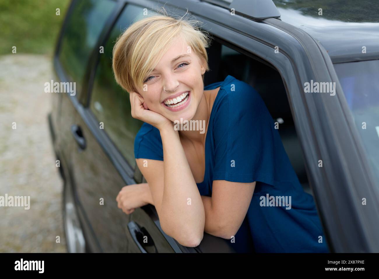 Giovane donna allegra che guarda fuori dal finestrino seduta in macchina Foto Stock