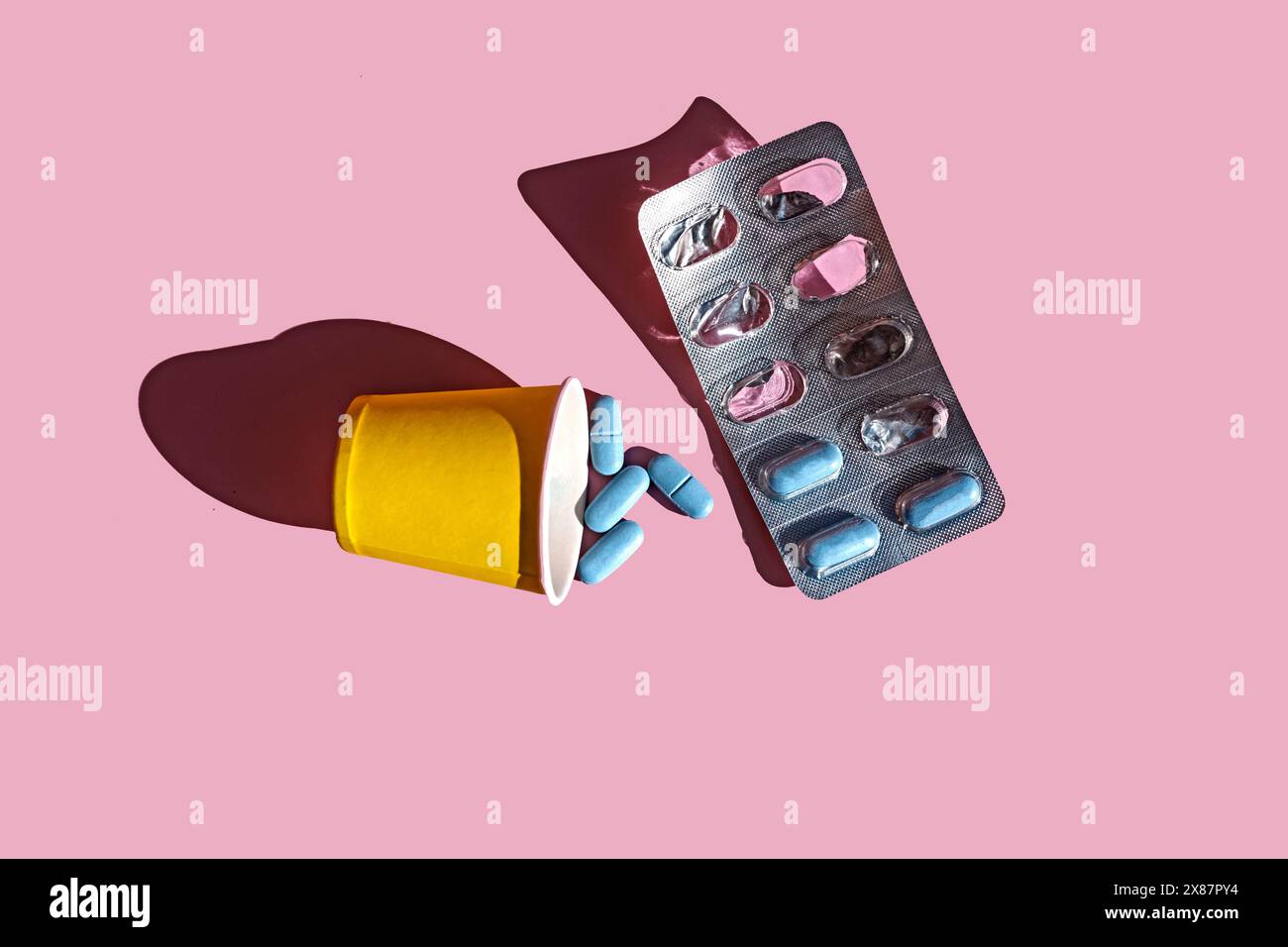 Tazza di carta con pillole blu e confezione blister su sfondo rosa Foto Stock
