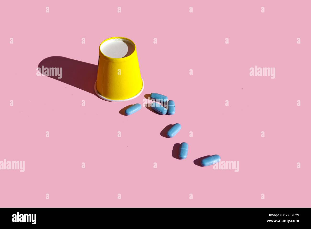 Tazza di carta gialla con pillole blu su sfondo rosa Foto Stock