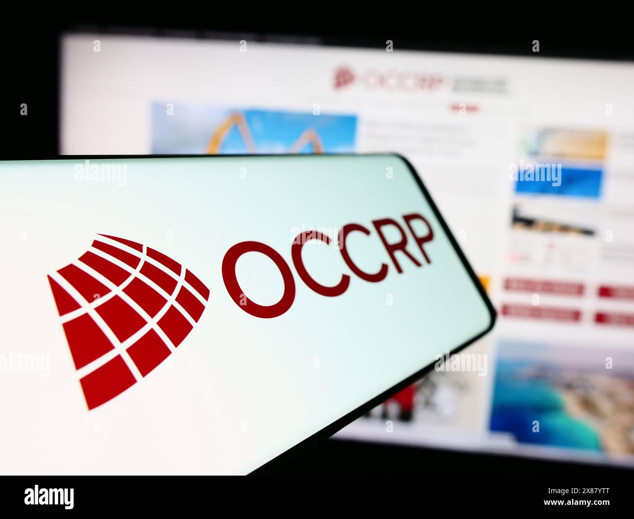 Smartphone con logo OCCRP (Organized Crime and Corruption Reporting Project) davanti al sito web. Mettere a fuoco la parte sinistra del display del telefono. Foto Stock