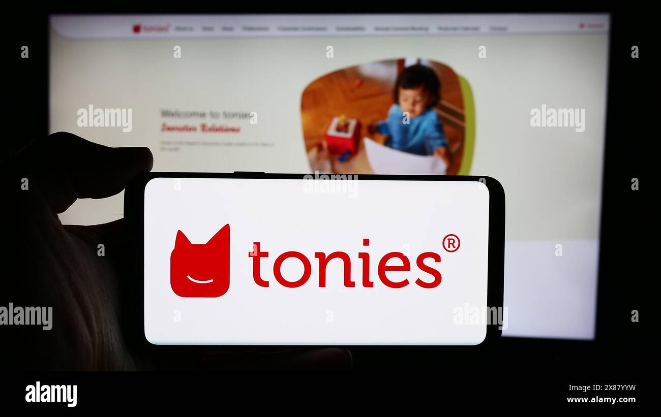 Persona che detiene un cellulare con il logo della società tedesca Tonies se (Toniebox) di fronte alla pagina web aziendale. Mettere a fuoco il display del telefono. Foto Stock