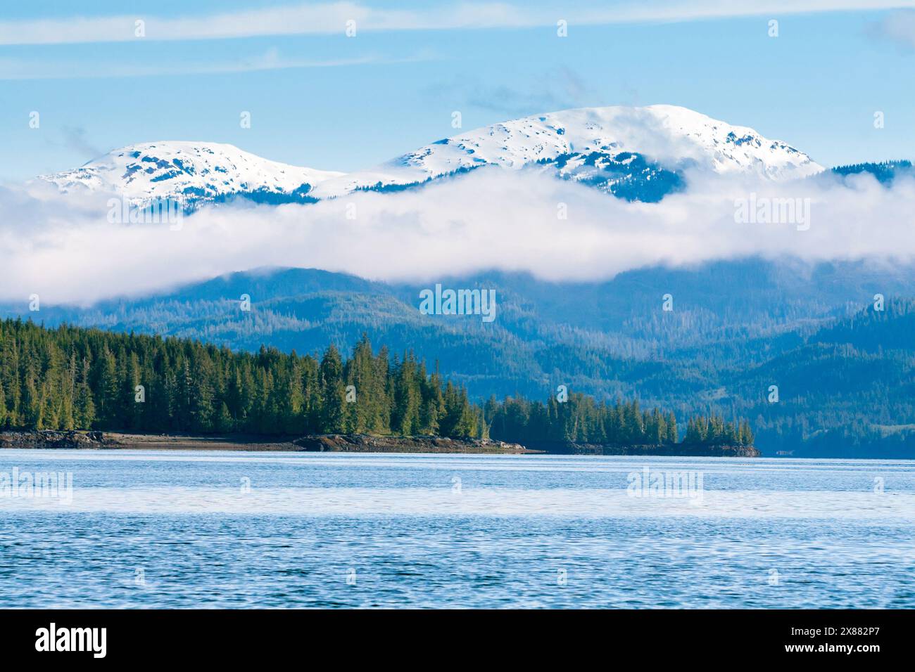 Nuvole sospese sulle montagne innevate e la foresta sempreverde lungo il Carroll Inlet vicino a Ketchikan, Alaska Foto Stock