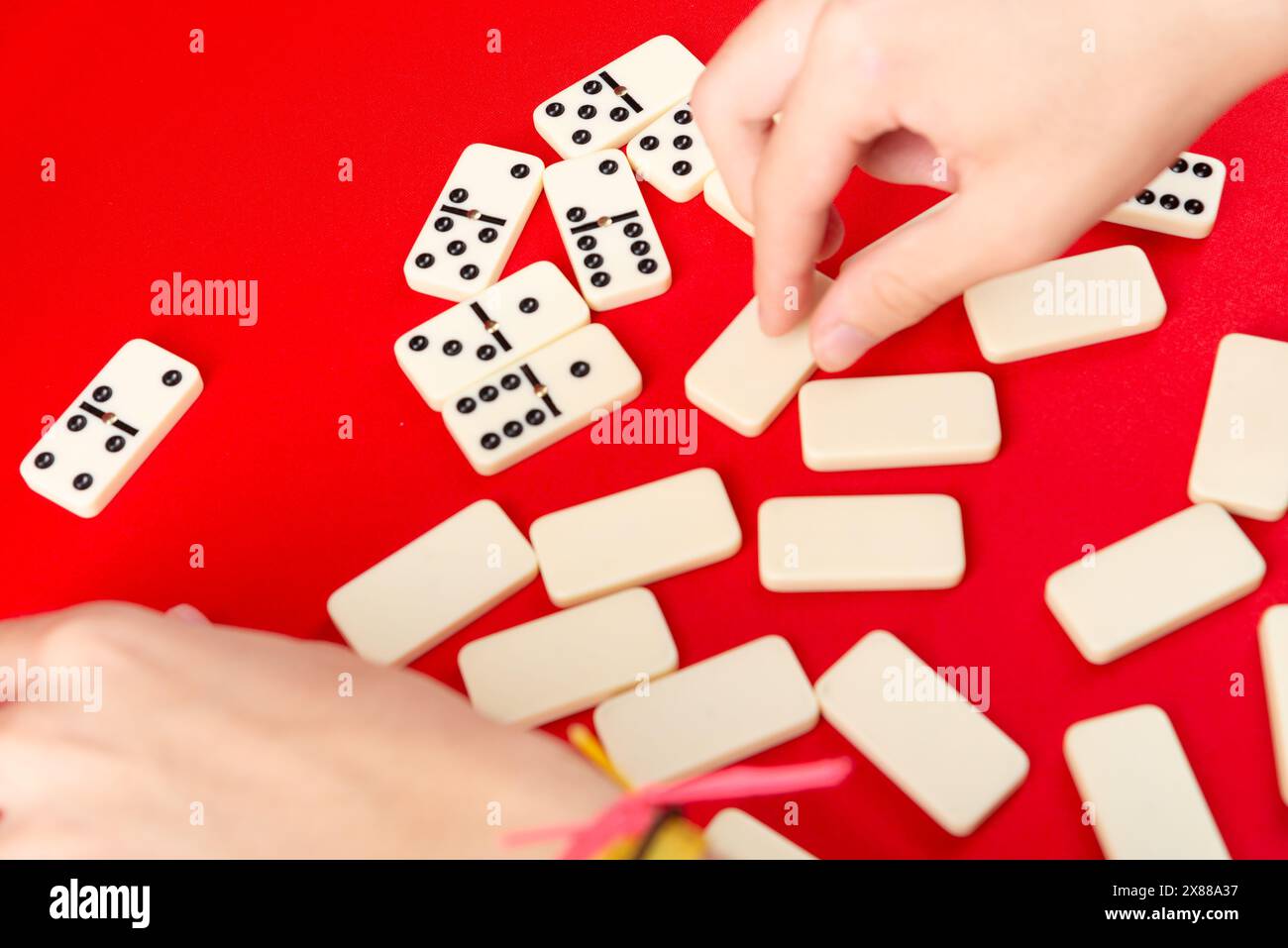 Mani maschili che mescolano domino. pezzi acrilici. Isolato su sfondo rosso. Foto Stock