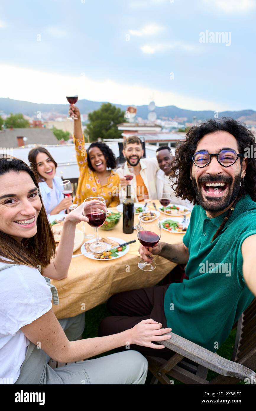 Gruppo di amici multirazziali che si divertono al party sul tetto. Uomo che prende selfie alla gente al barbecue. Foto Stock