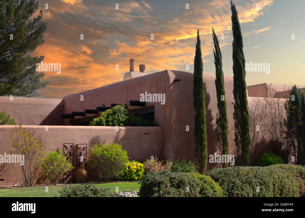 Vicino al tramonto incornicia l'imponente casa in stile revival Pueblo con pareti in mattoni di adobe, alberi di cipressi e giardini a Las Cruces, NEW MEXICO Foto Stock