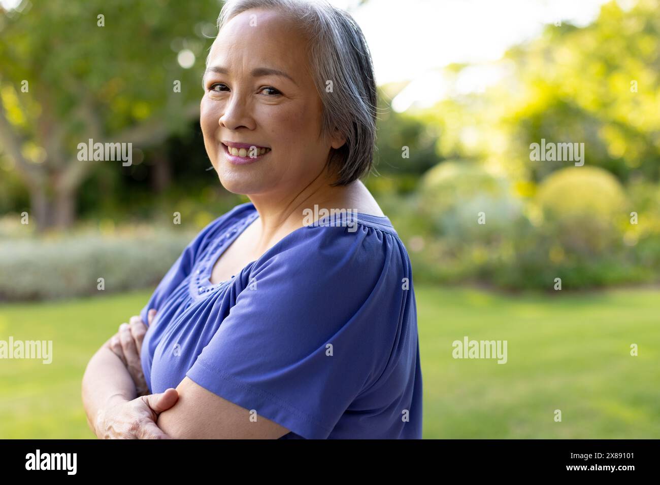 Una donna asiatica di mezza età con i capelli grigi corti sorride all'aperto Foto Stock