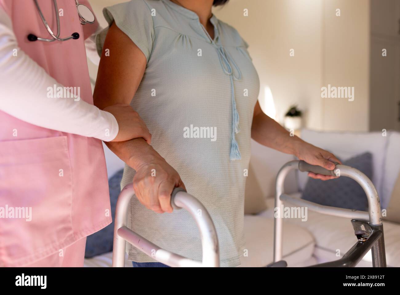 A casa, la giovane infermiera asiatica e la paziente di mezza età stanno usando il walker Foto Stock