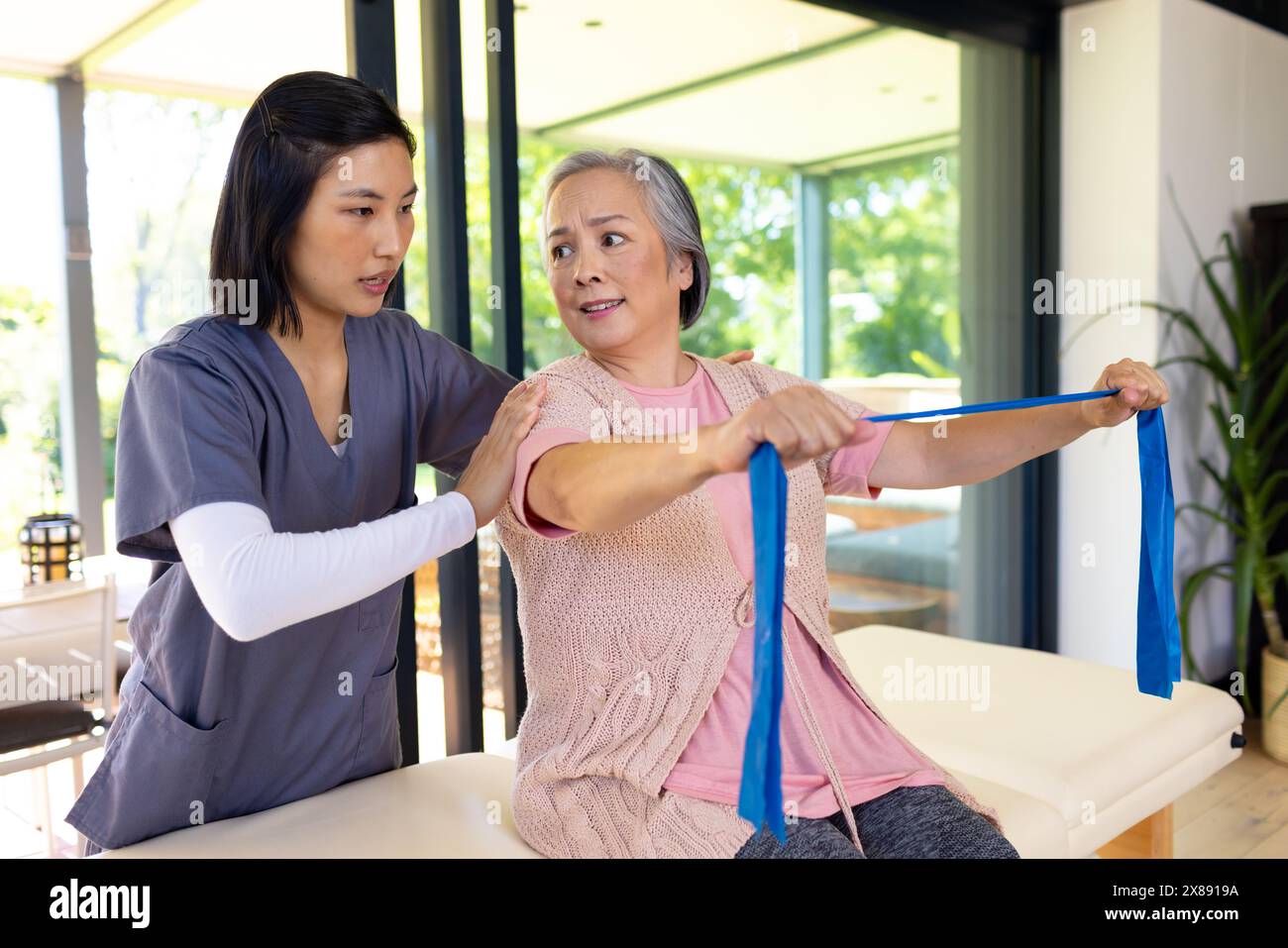 A casa, giovane infermiera asiatica e paziente di mezza età che esercita Foto Stock
