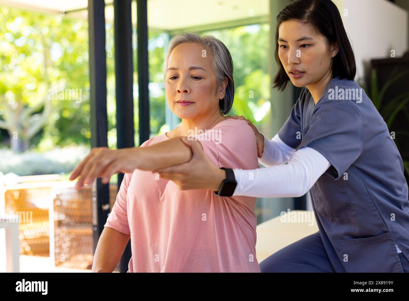 A casa, giovane infermiera asiatica e paziente di mezza età che allunga le braccia Foto Stock