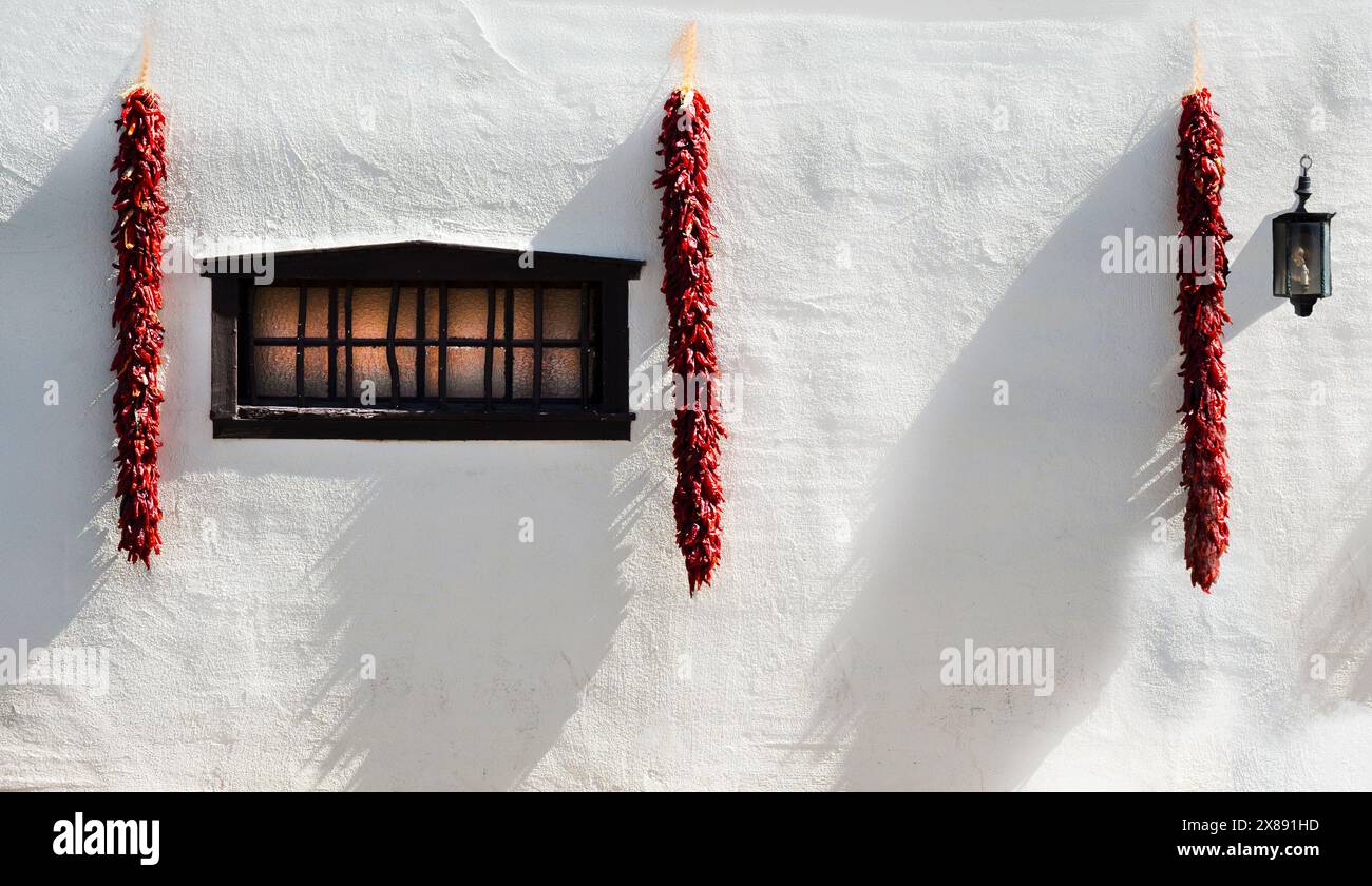 Illuminazione laterale dei ristrati rossi di peperoncino appesi su una parete bianca all'esterno della tradizionale dimora del New Mexico meridionale a Mesilla, NEW MEXICO, USA Foto Stock