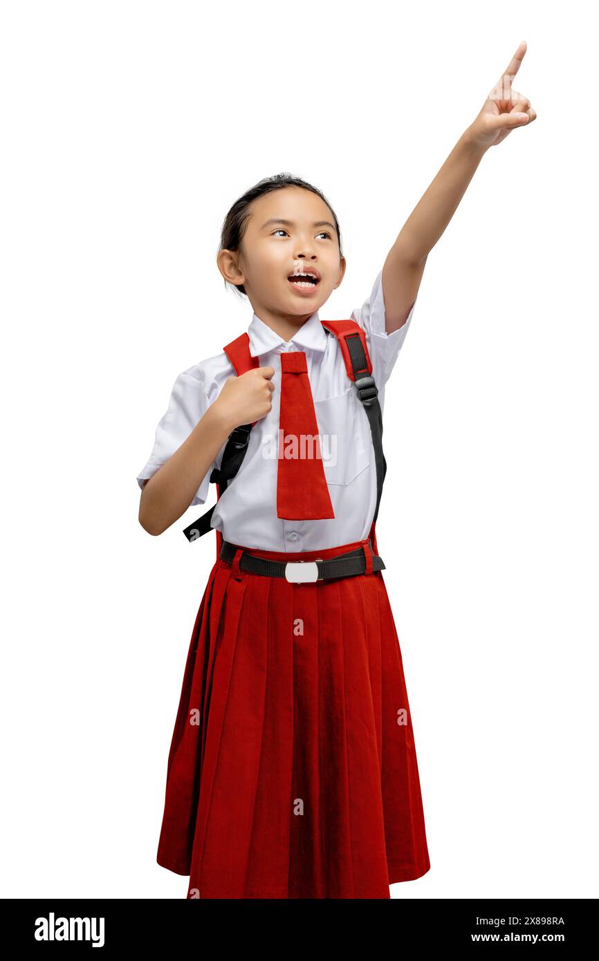 Eccitata studentessa elementare con gonna rossa e camicia bianca rivolta verso l'alto con curiosità ed entusiasmo. Mostrando la sua aspirazione all'apprendimento e. Foto Stock
