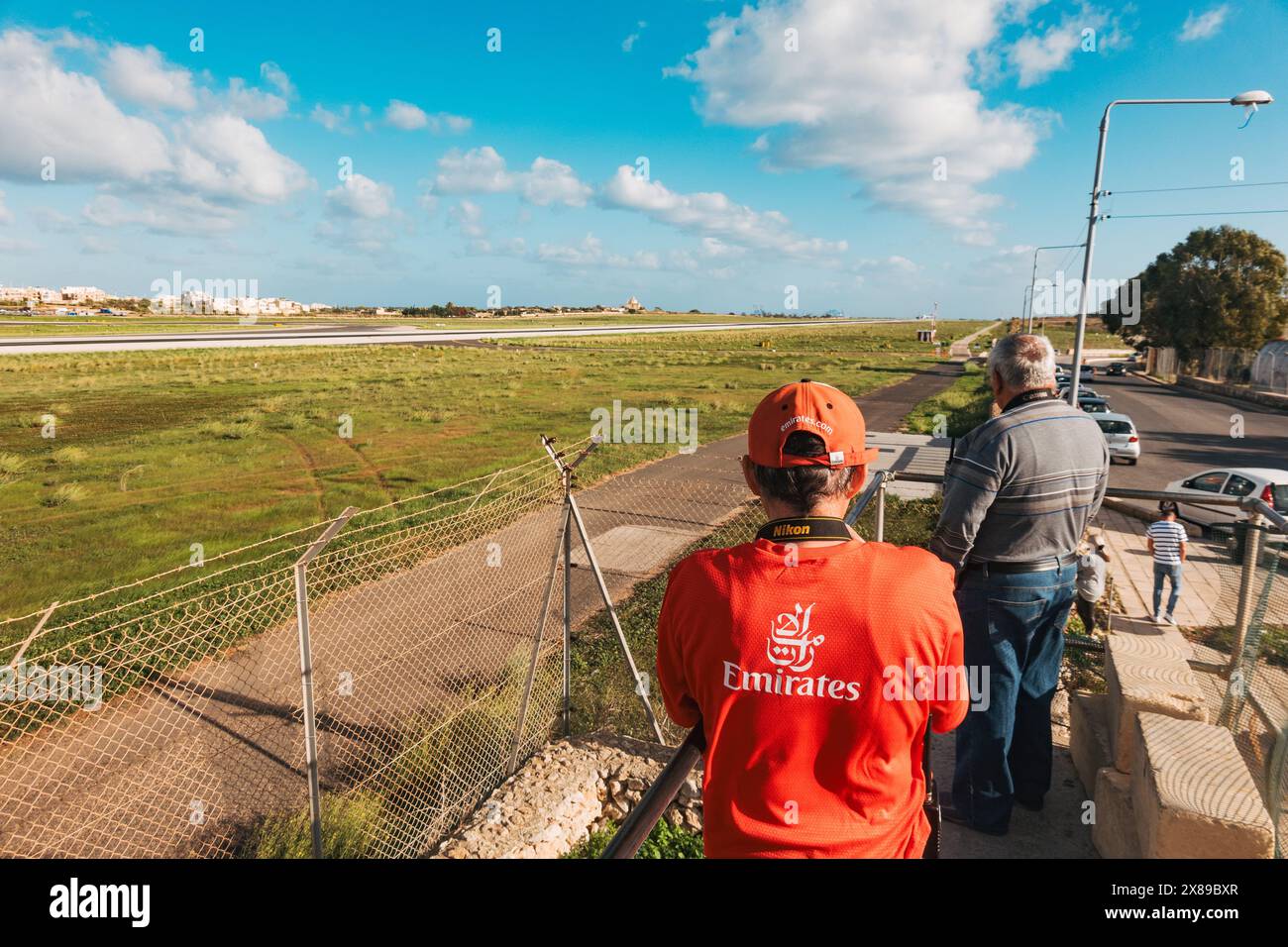 Planespotters, uno che indossa un abbigliamento a tema Emirates, pronto a fotografare un aereo mentre decolla dall'aeroporto internazionale di Malta Foto Stock