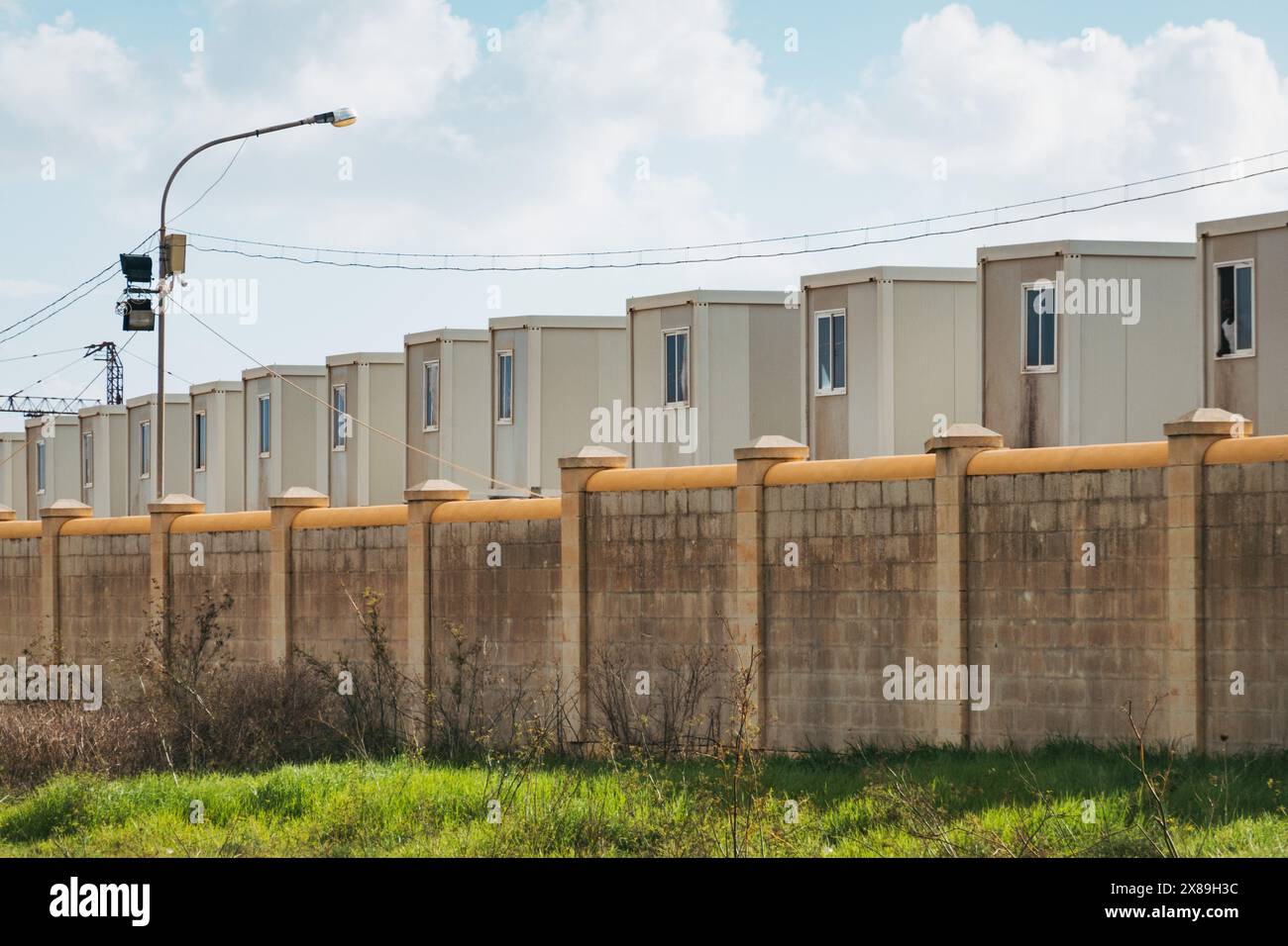 Unità abitative container dietro un muro presso il Centro aperto Ħal far, una struttura abitativa per migranti e richiedenti asilo a Malta Foto Stock