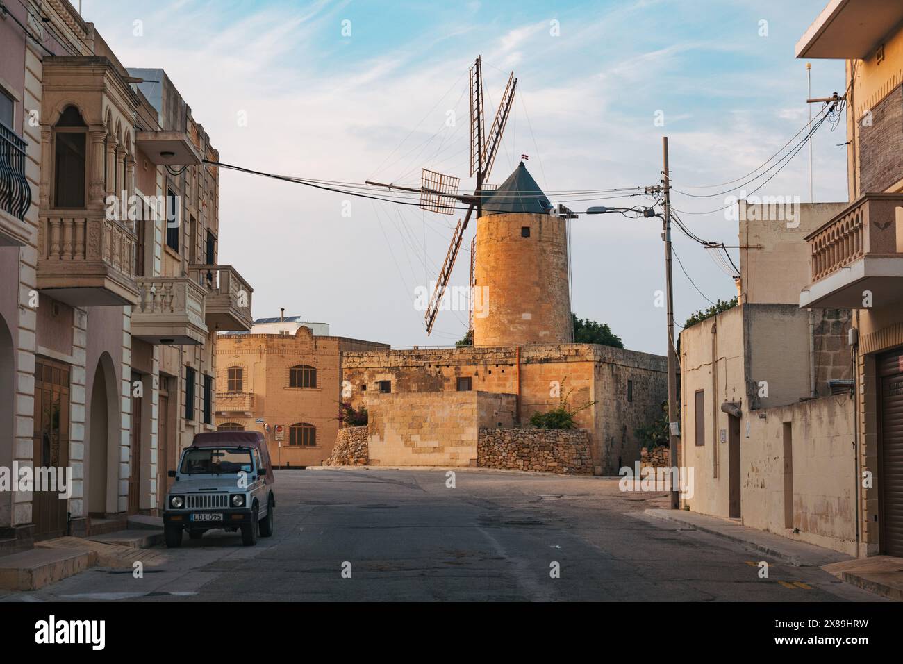 Un piccolo mulino a vento torreggia su una strada residenziale in una piccola città sull'isola di Gozo, Malta Foto Stock