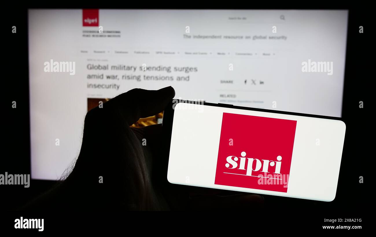 Persona che possiede un telefono cellulare con il logo del Stockholm International Peace Research Institute (SIPRI) di fronte alla pagina web. Mettere a fuoco il display del telefono. Foto Stock