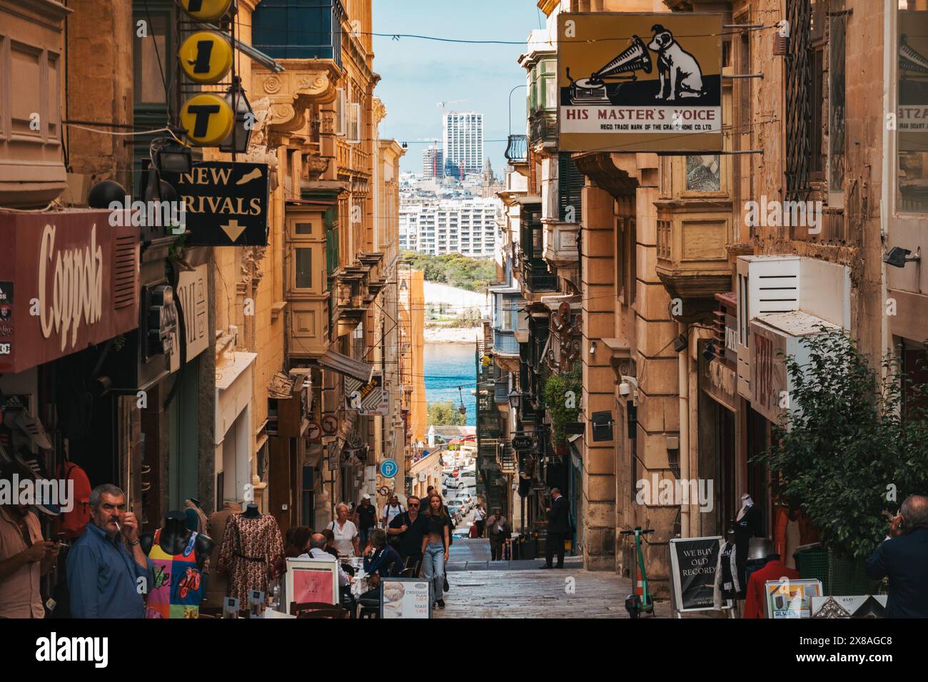 I visitatori passeggiano lungo una vivace strada di la Valletta, circondata da edifici storici e con vista sul porto Foto Stock