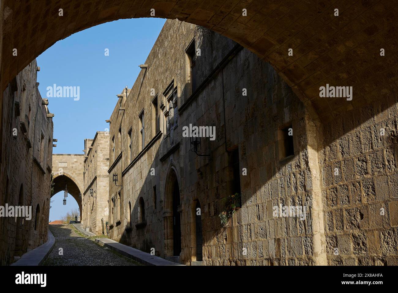 Sentiero in pietra sotto un arco, circondato da edifici storici medievali all'ombra, via dei Cavalieri, città vecchia di Rodi, città di Rodi, Rodi, Dodecaneso, GRE Foto Stock