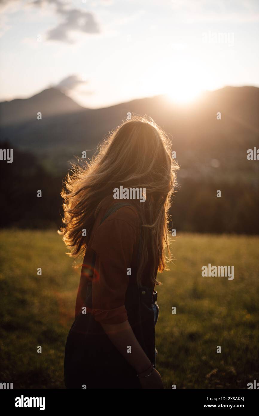 Donna Bruna con capelli fluenti al tramonto nel prato con le montagne Foto Stock