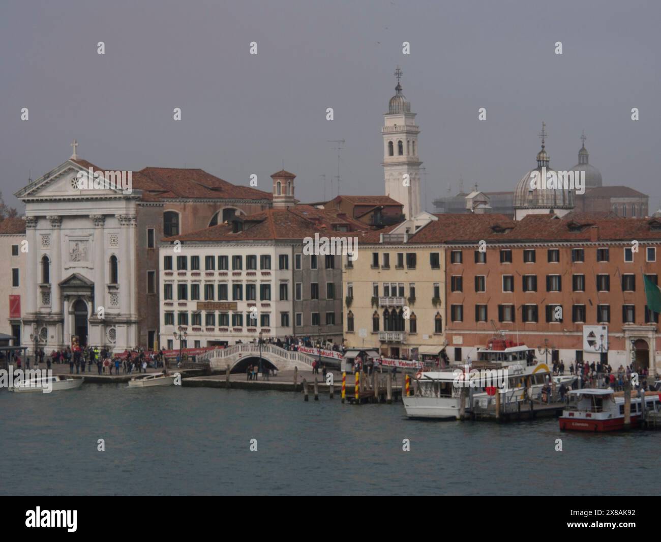 Un gruppo di edifici tra cui una chiesa accanto a un canale con turisti e barche, edifici storici con portici e cupole su un canale in italia, Veni Foto Stock