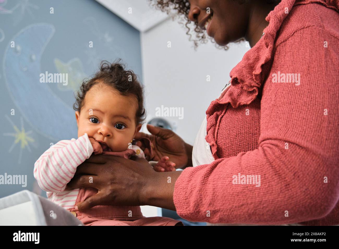 La madre africana tiene in braccio una bambina mentre si cambia i vestiti. Foto Stock