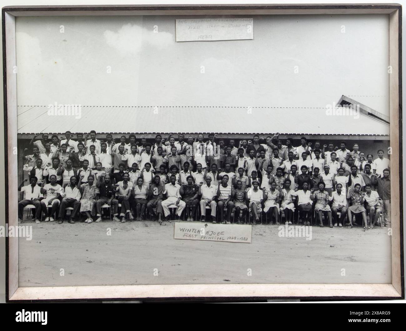 Artefatti del Solomon Mahlangu Freedom College (SOMAFCO). Foto di gruppo in bianco e nero incorniciata di 101 persone. Titolo recita: ANC Solomon Mahlangu Colleg (sic) primo staff & studenti 1979 Nota con freccia punta a: Wintshi Njobe, primo preside 1979-1982 sulla scia della rivolta dei giovani a Soweto e in altre città del Sud Africa del 1976, l'ANC istituì il Solomon Mahlangu Freedom College (SOMAFCO) a Mazimbu vicino alla città di Morongoro, Tanzania, su terreni donati dal governo tanzaniano. Il College fu il risultato del lavoro del comitato educativo dell'ANC a Londra per Pione Foto Stock