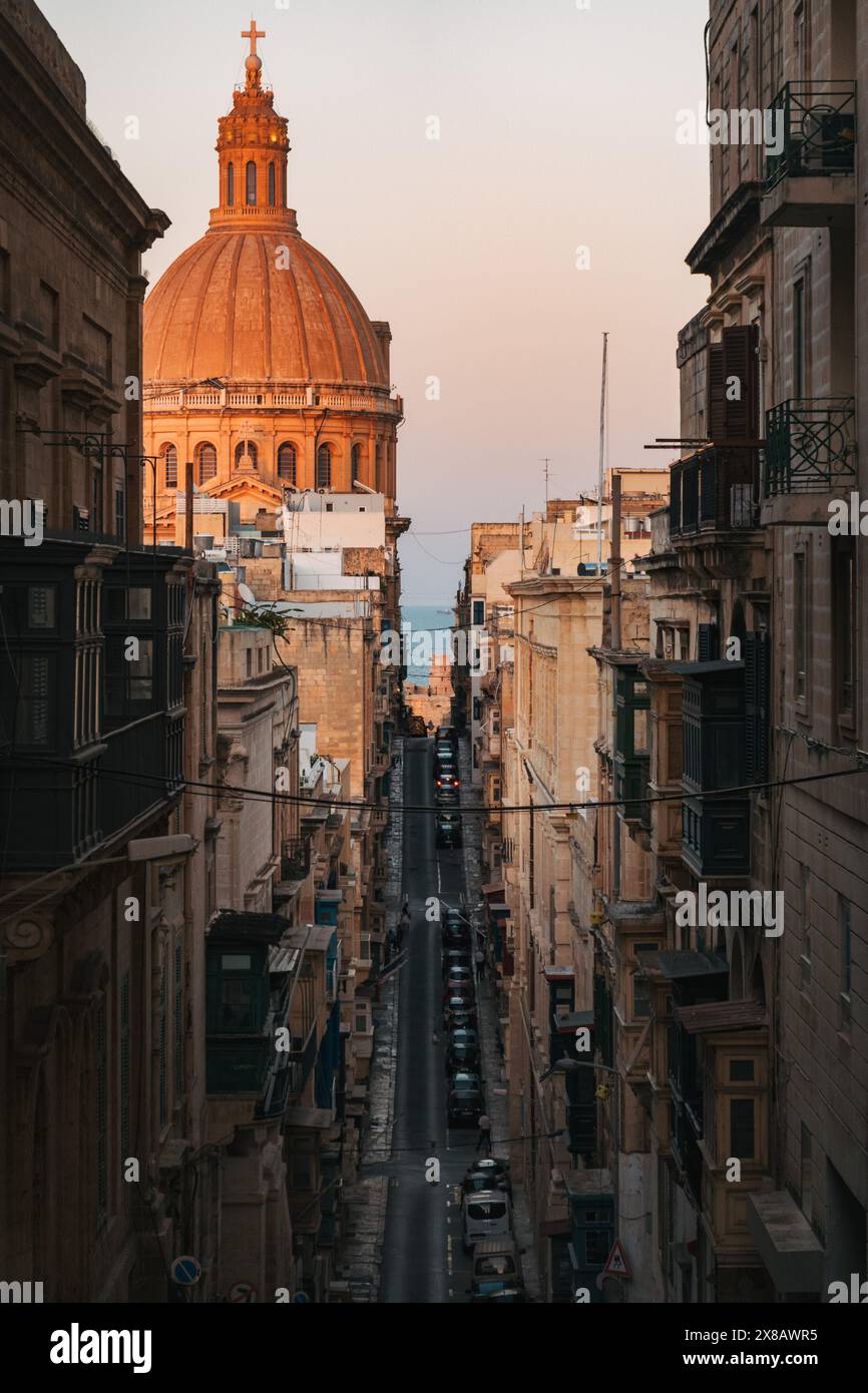 Le strette stradine di la Valletta mostrano una splendida architettura e un assaggio di una cupola arancione della cattedrale di San Paolo alla luce della sera Foto Stock