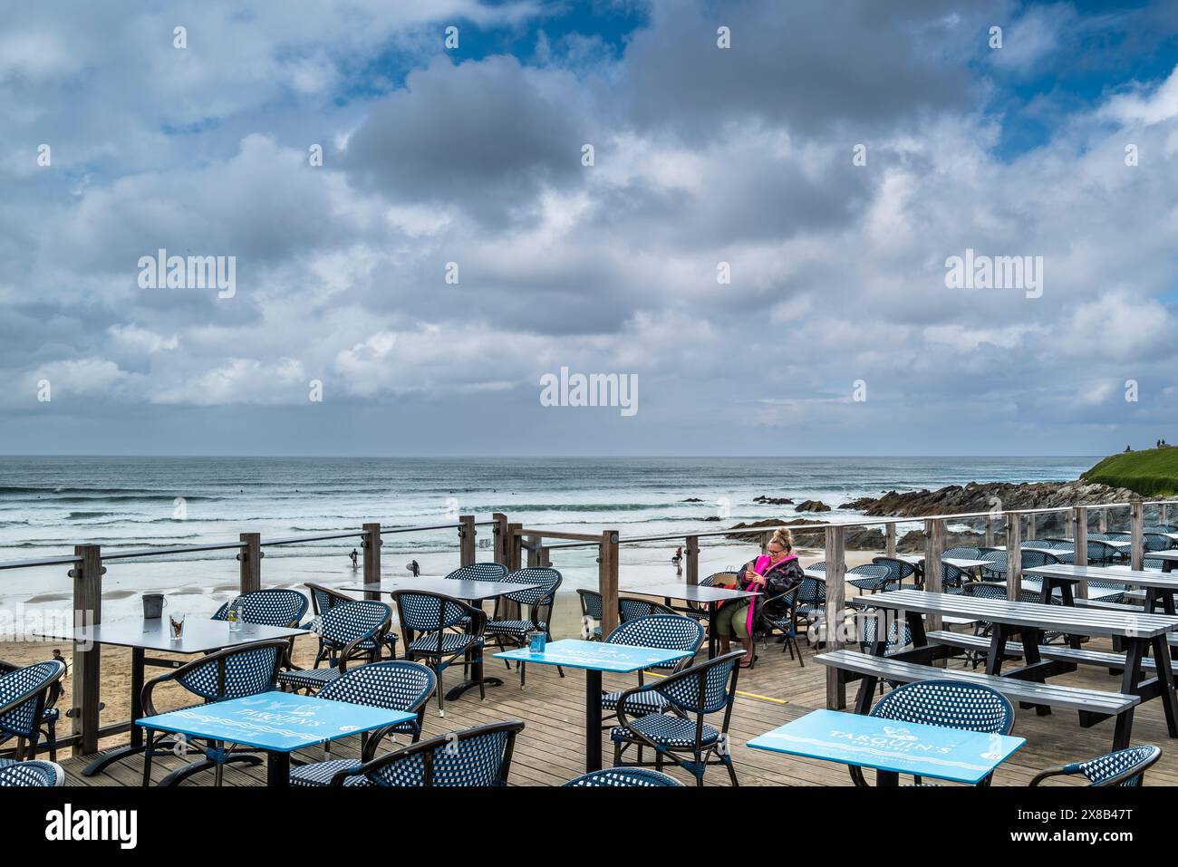 Una vacanziera seduto da sola a un tavolo con il suo smartphone nell'area coperta esterna dell'area del Fistral Beach Bar presso la spiaggia di Fistral a Newqu Foto Stock