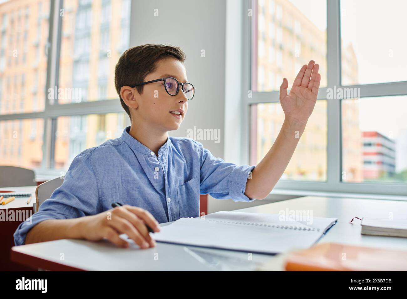 Un giovane con la mano in alto, coinvolge attivamente gli studenti in un ambiente luminoso e vivace in classe. Foto Stock