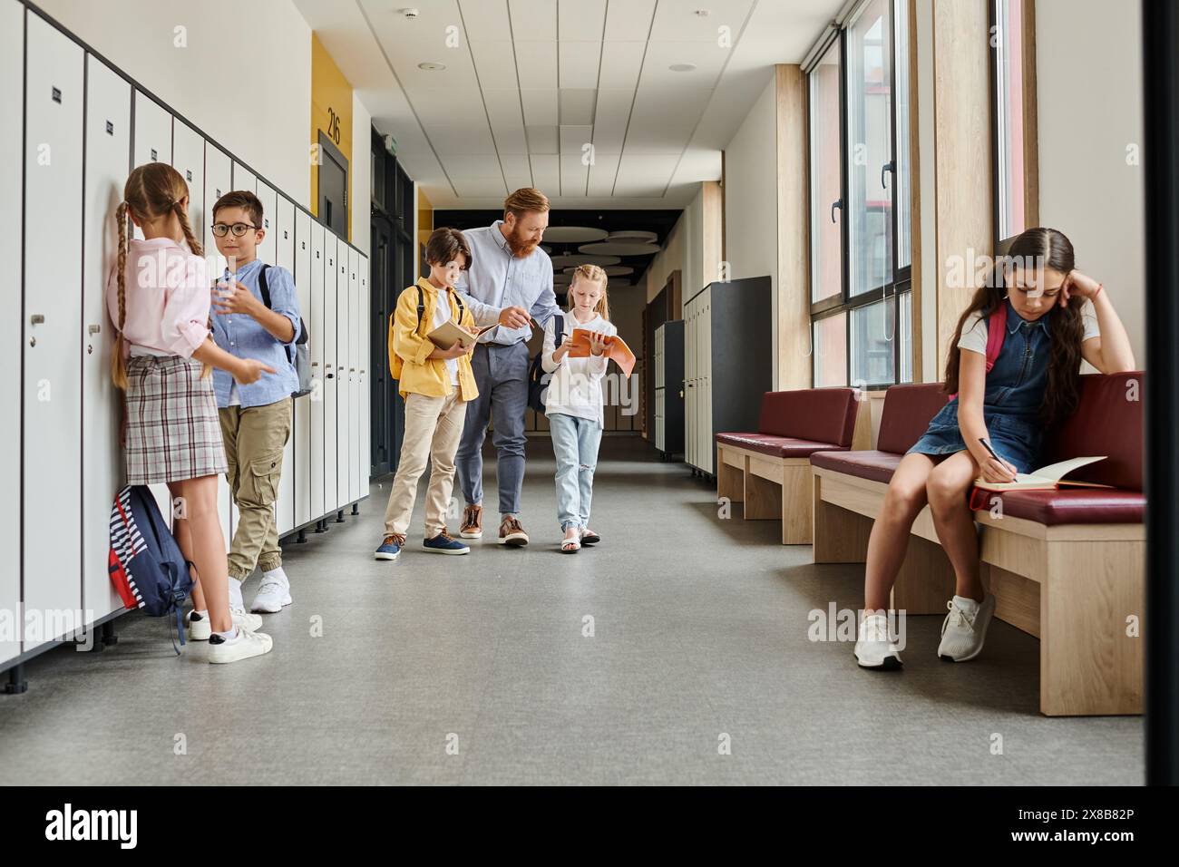 Un gruppo di individui, tra cui un insegnante uomo, in piedi in un corridoio vicino a armadietti, impegnati in conversazione e istruzione. Foto Stock