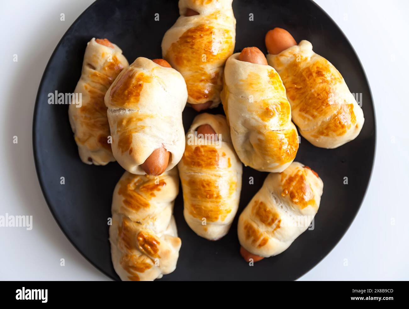 Salsicce nell'impasto su un piatto di ceramica sul tavolo. Foto Stock