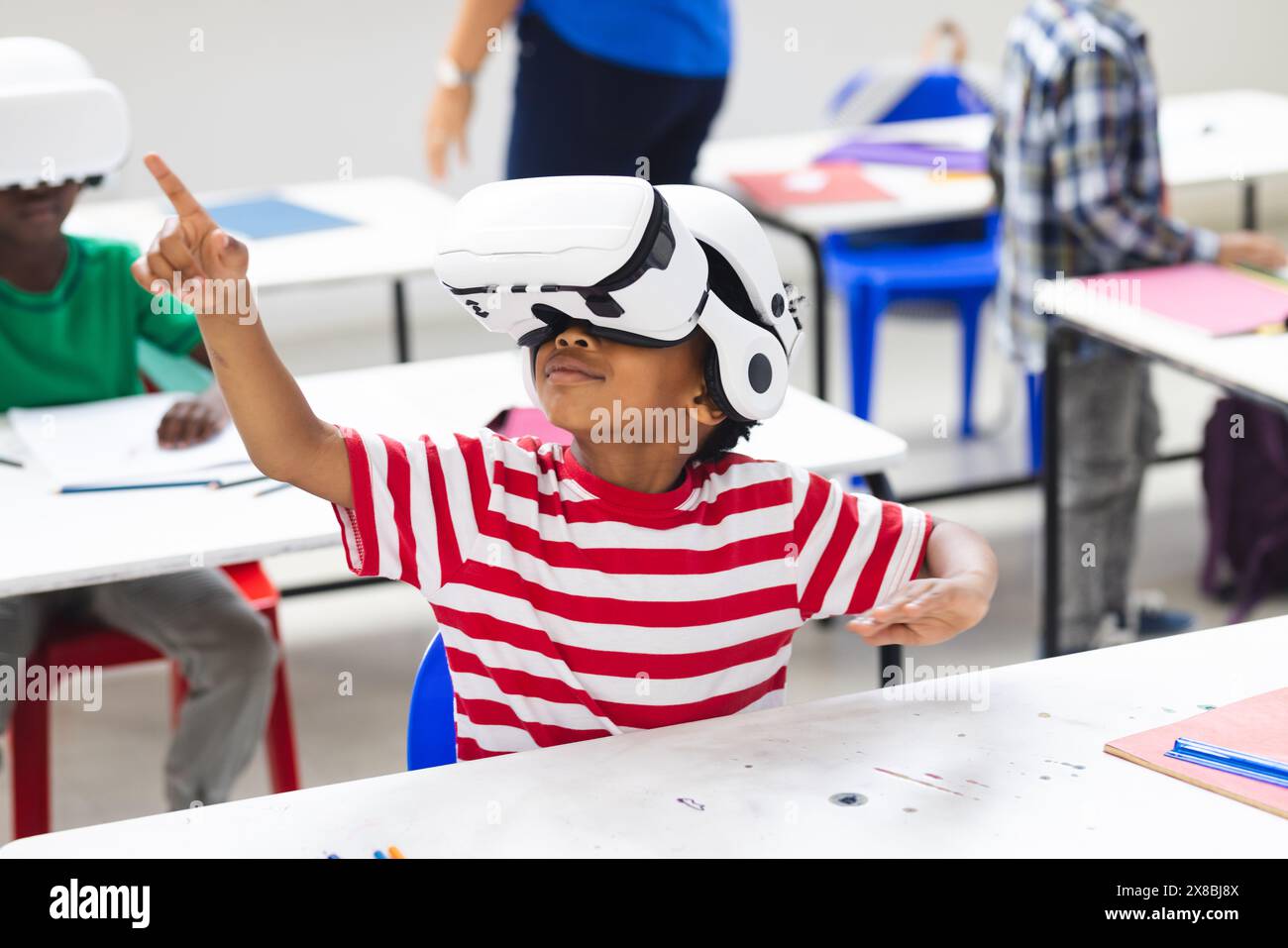 In classe scolastica, ragazzo birazziale che indossa il visore per la realtà virtuale rivolto verso l'alto Foto Stock