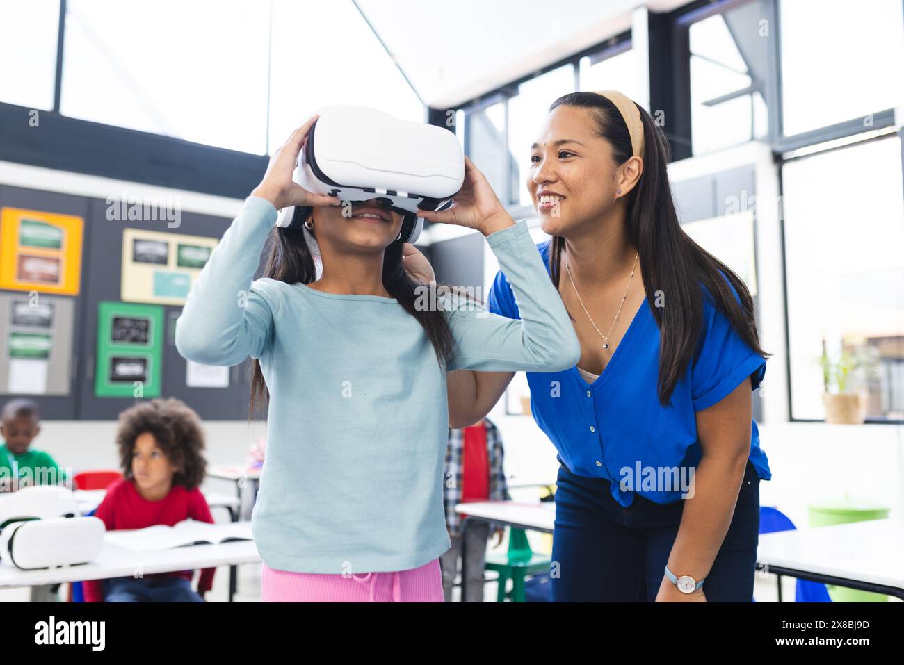 Una donna asiatica di mezza età assiste una giovane ragazza con un visore VR Foto Stock