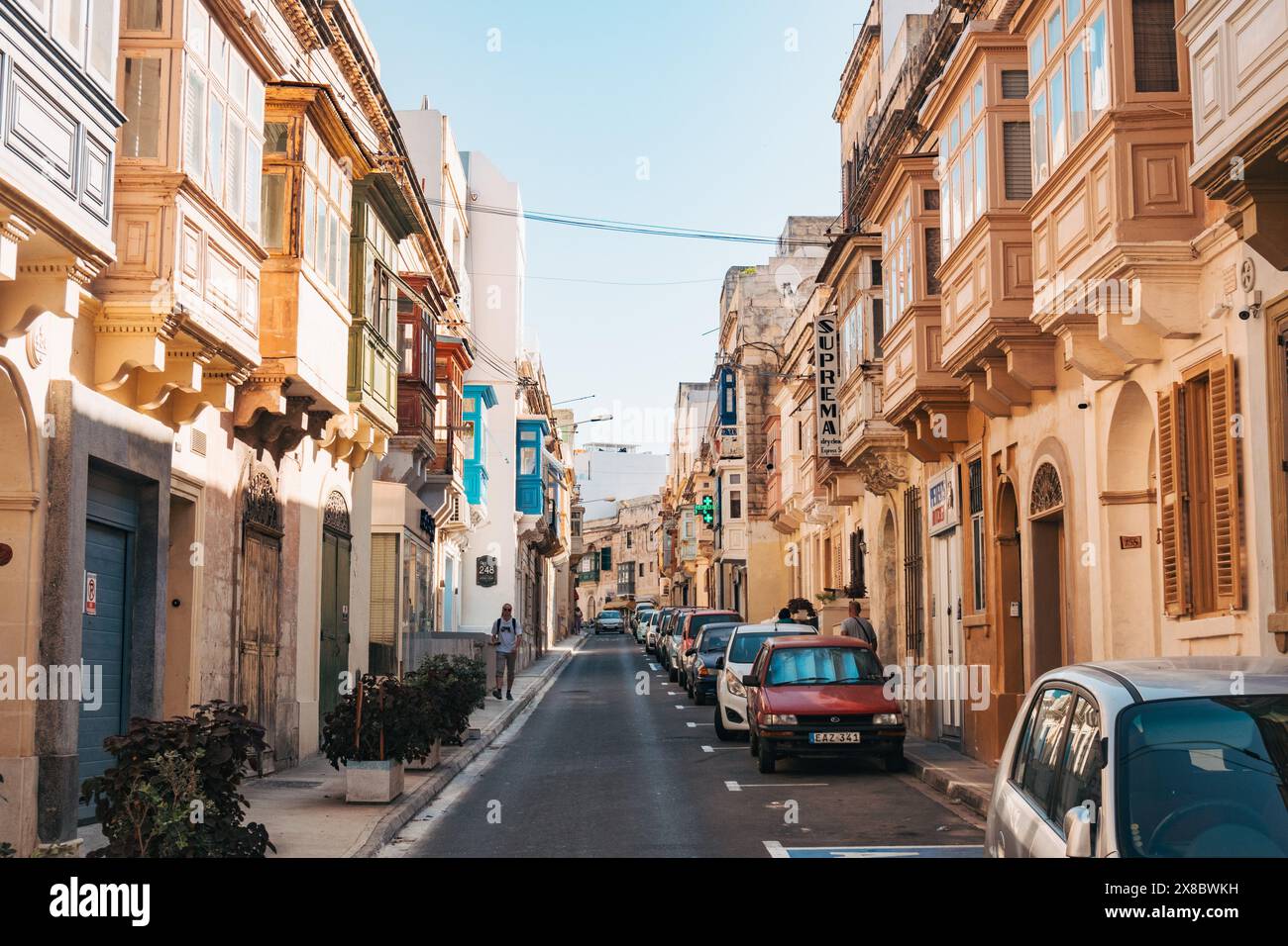 Una strada stretta fiancheggiata da case in pietra calcarea e balconi in legno con finestre nella città di Sliema, Malta Foto Stock