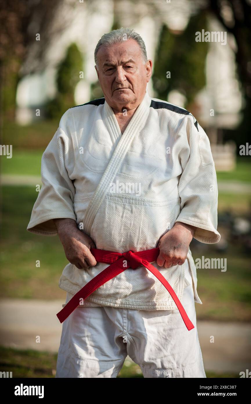Il maestro delle arti marziali Un esperto sensei in un kimono bianco regge una vivace cintura rossa, incarnando l'essenza della maestria e dell'esperienza nel judo, aikid Foto Stock