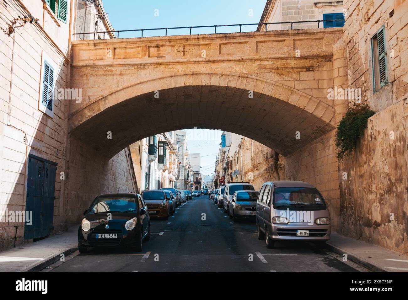 Auto compatte parcheggiate in una strada stretta sotto un ponte nella città di Sliema, Malta Foto Stock